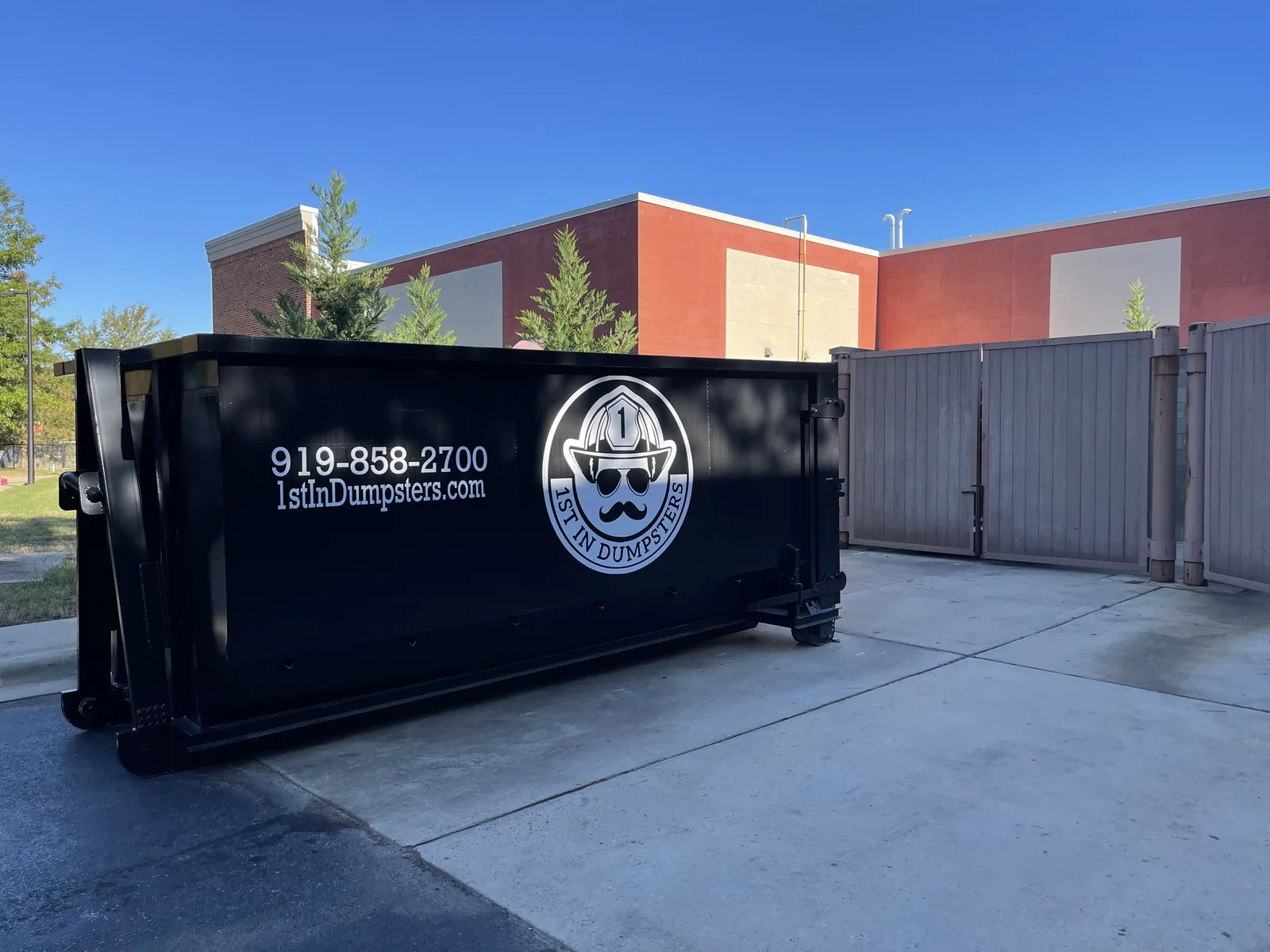 Black 1st In Dumpsters roll off dumpster on a concrete lot beside a brick building